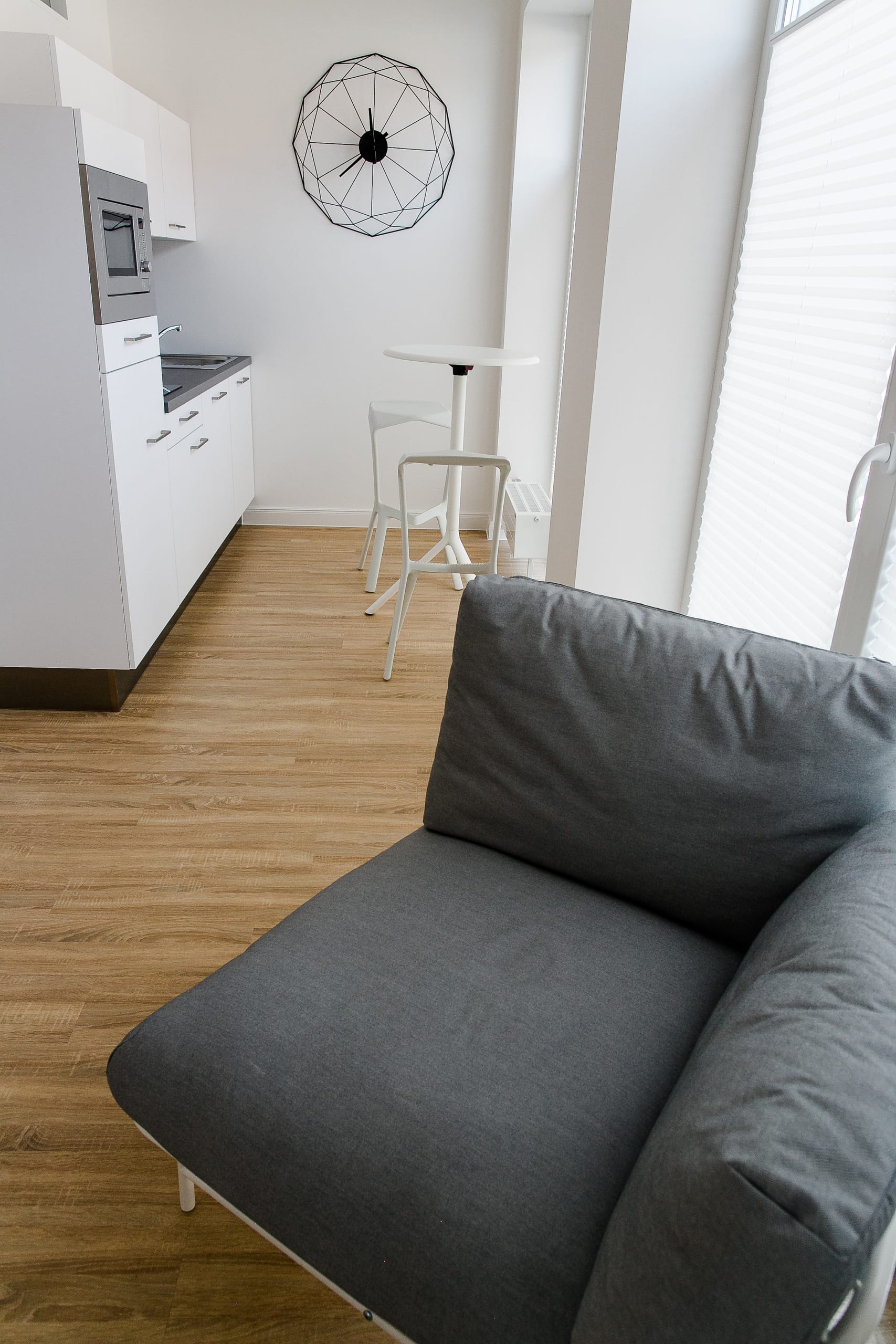 Modernes Apartment, Küchenzeile mit Mikrowelle, Wanduhr, Holzboden und graues Sofa