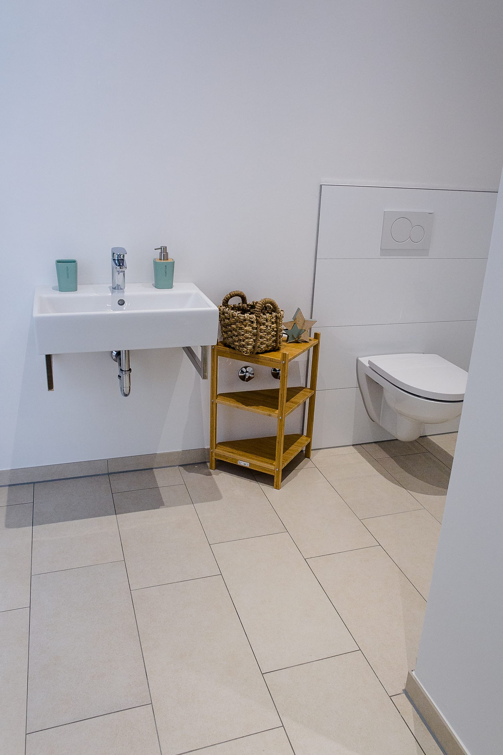 Modernes Badezimmer mit weißem Waschbecken, Toilettenschüssel und einem kleinen Holzregal