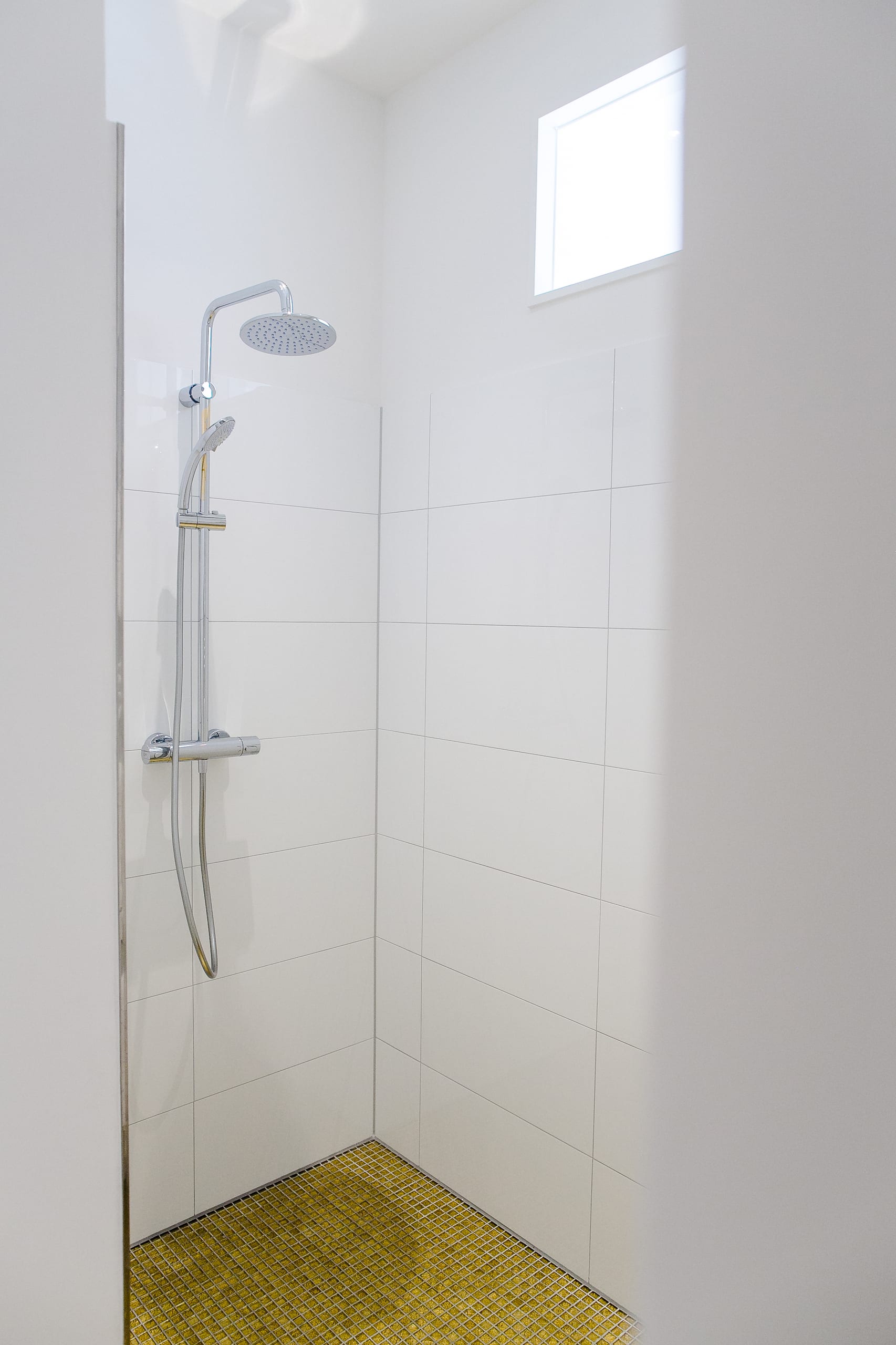 Dusche mit weiß gefliesten Wänden, goldenem Mosaikboden und kleinem Fenster