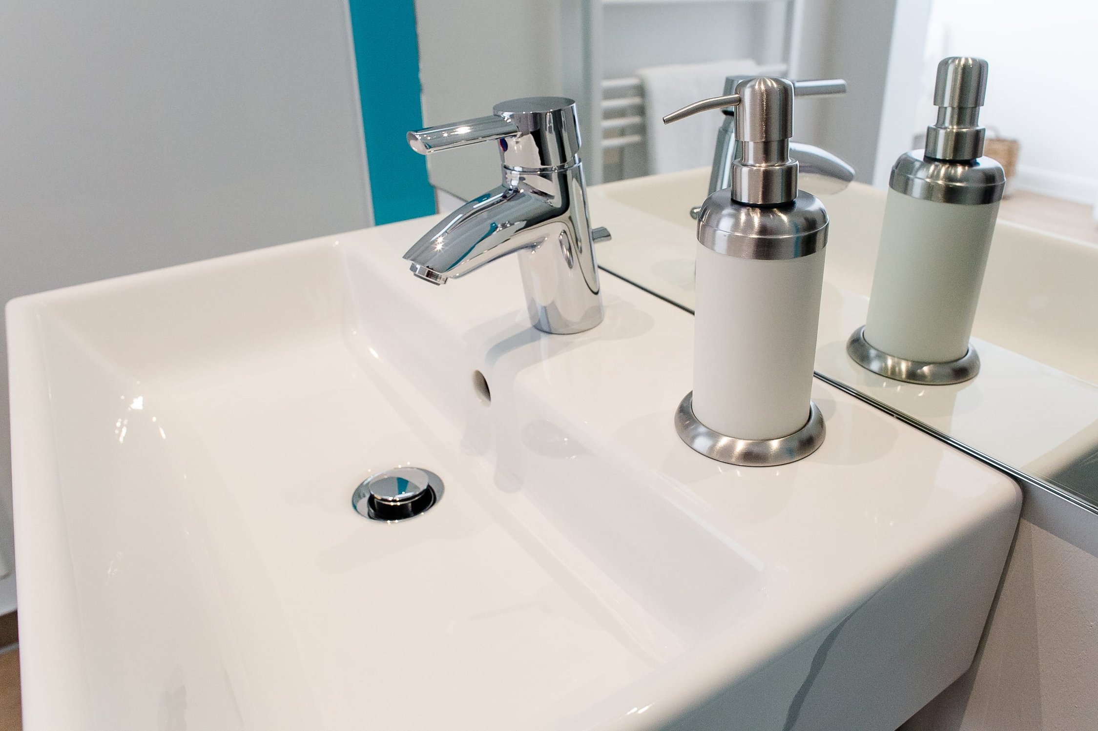 Weißes Waschbecken mit Chromarmatur, Spender in Weiß und Silber, Wand mit blauen Akzenten