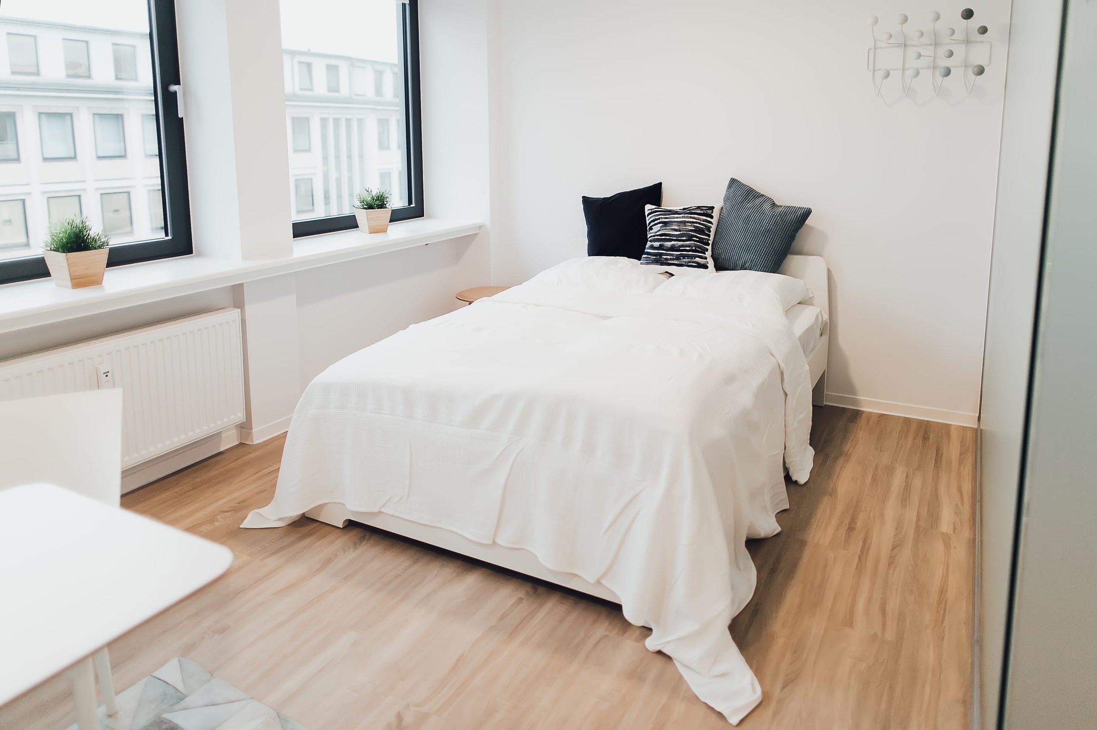 Schlafzimmer mit weißem Bett, Fenster zur Stadt und hellem Holzfußboden