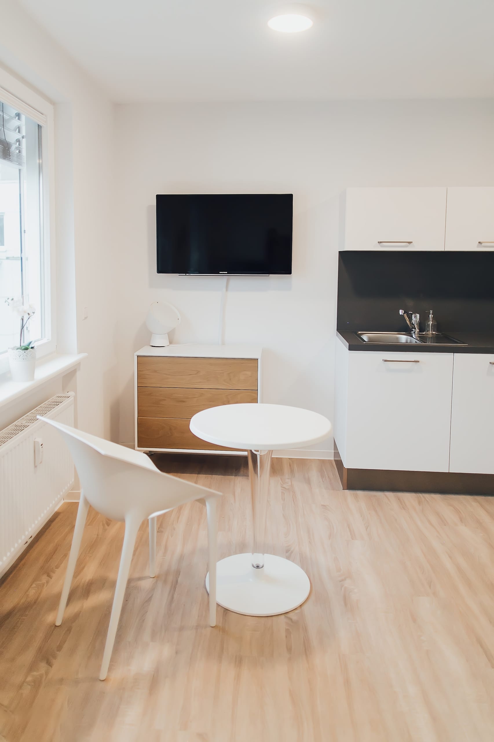 Kleiner Wohnraum mit minimalistischer Einrichtung, heller Holzboden, weißer Stuhl, runder Tisch