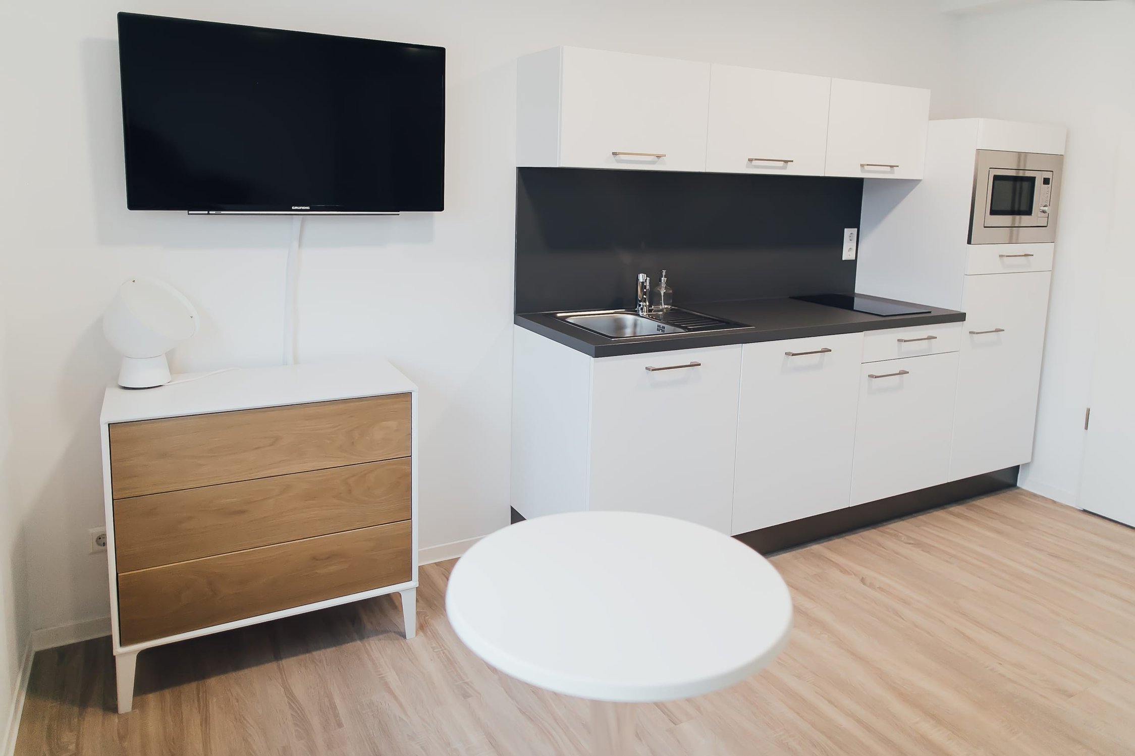 Moderne Küchenzeile in Weiß mit Spüle und Mikrowelle, Holzkommode und Fernseher