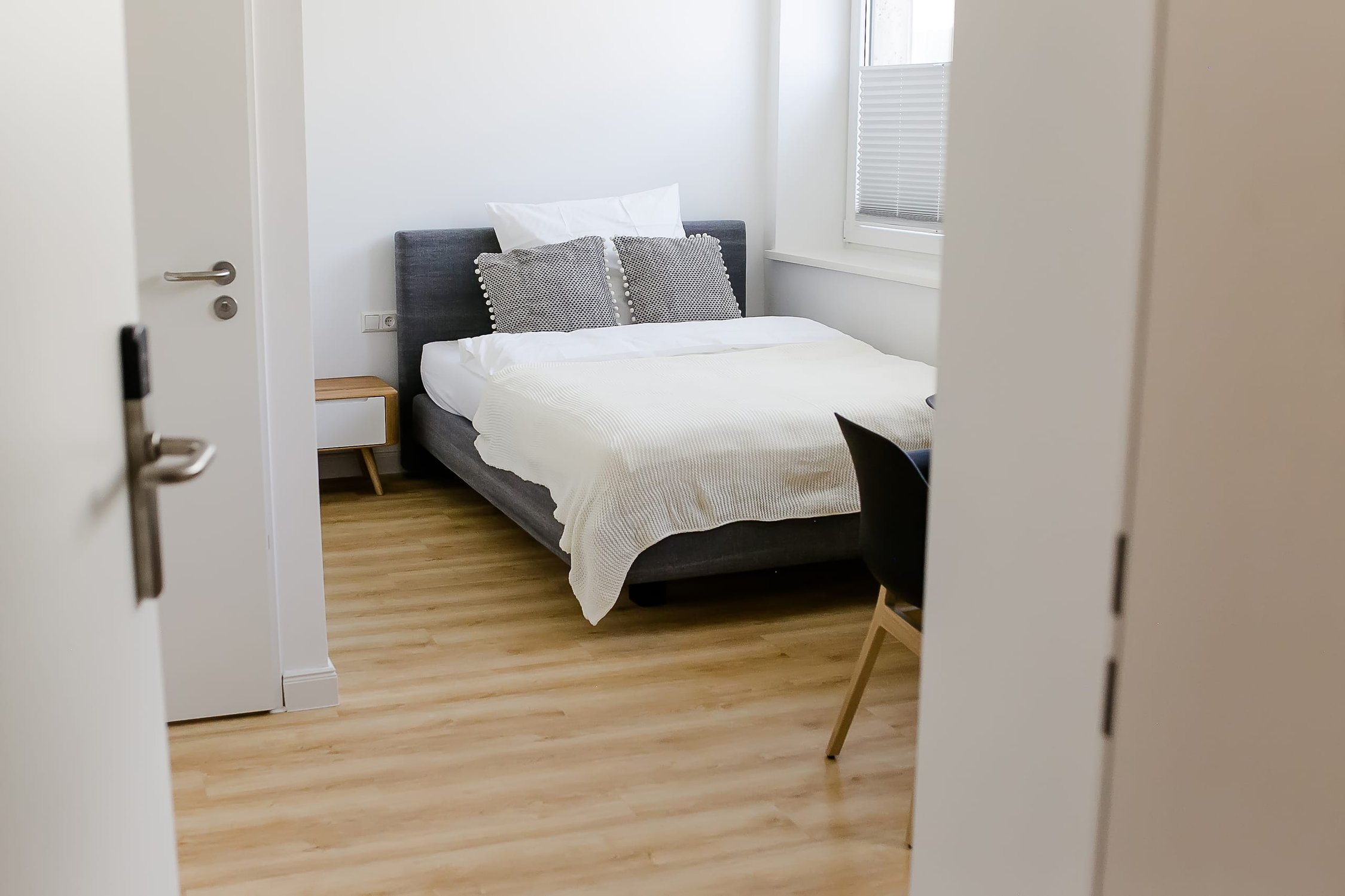 Schlafzimmer mit weißem Bett, grauer Polsterung, zwei Kissen und heller Holzoptik-Boden