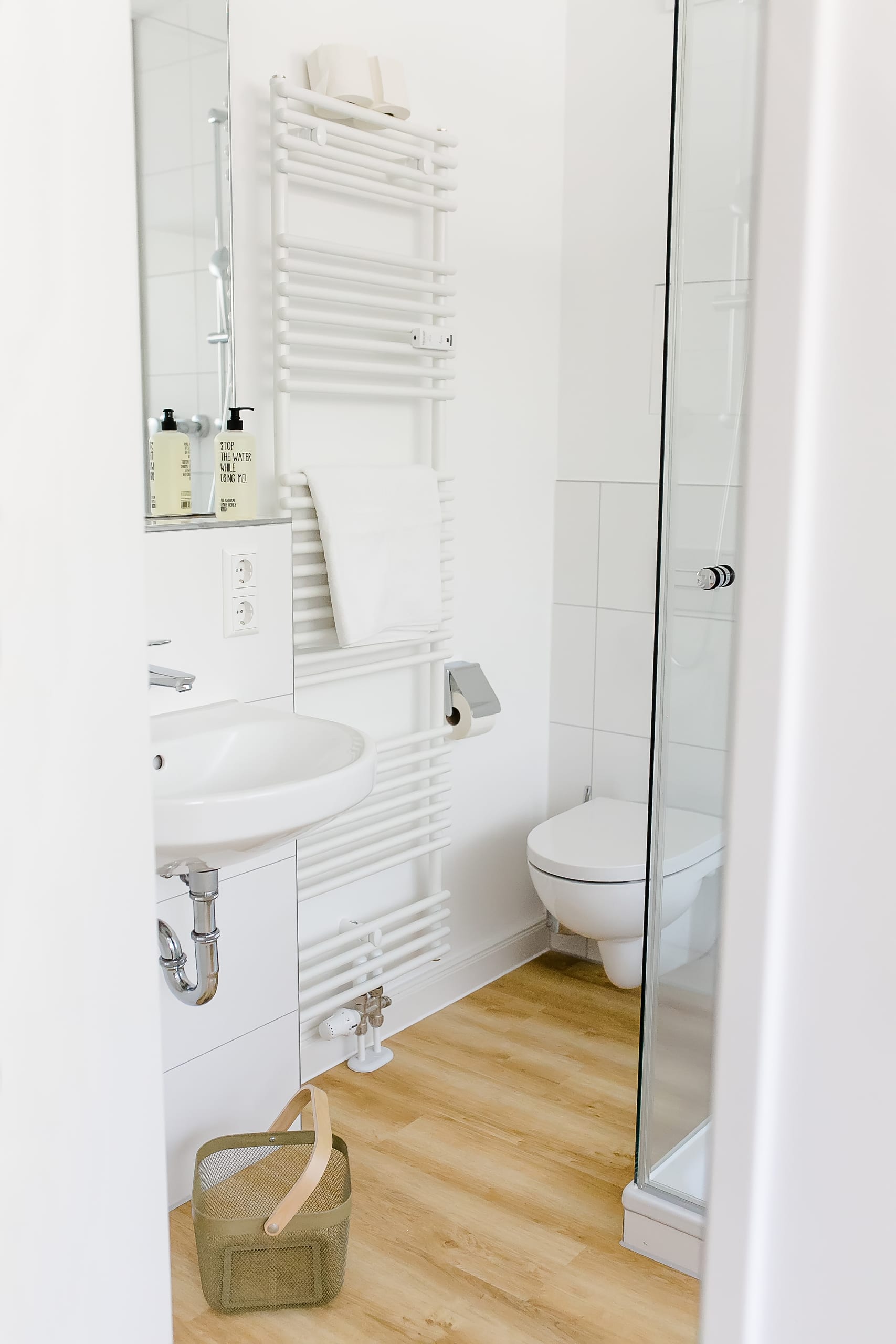 Schmales Badezimmer mit weißem Waschbecken, Heizkörper und Toilette, heller Holzfußboden
