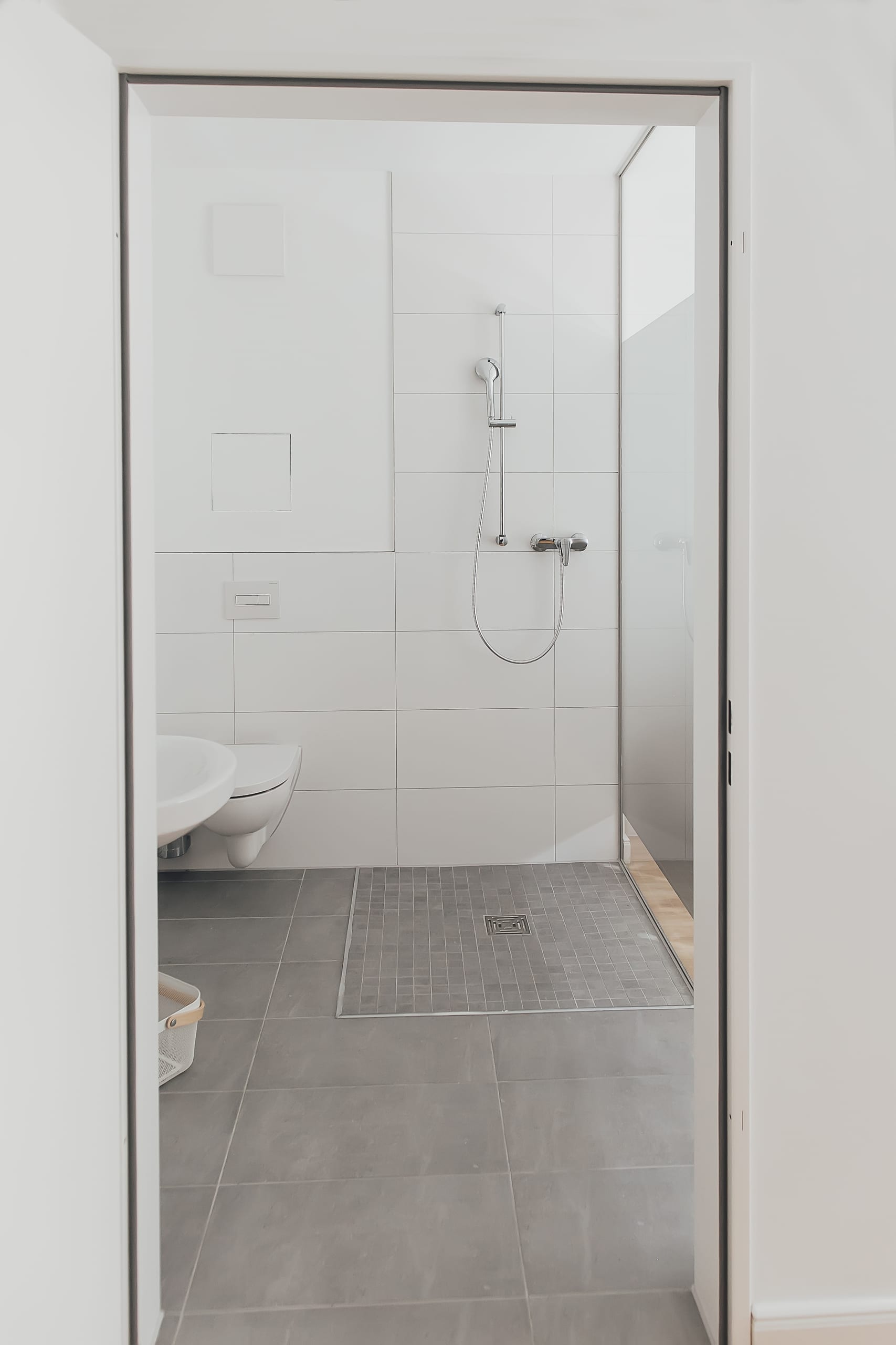 Badezimmer mit weißer Toilette, Duschkopf und grauen Fliesen, heller Raum