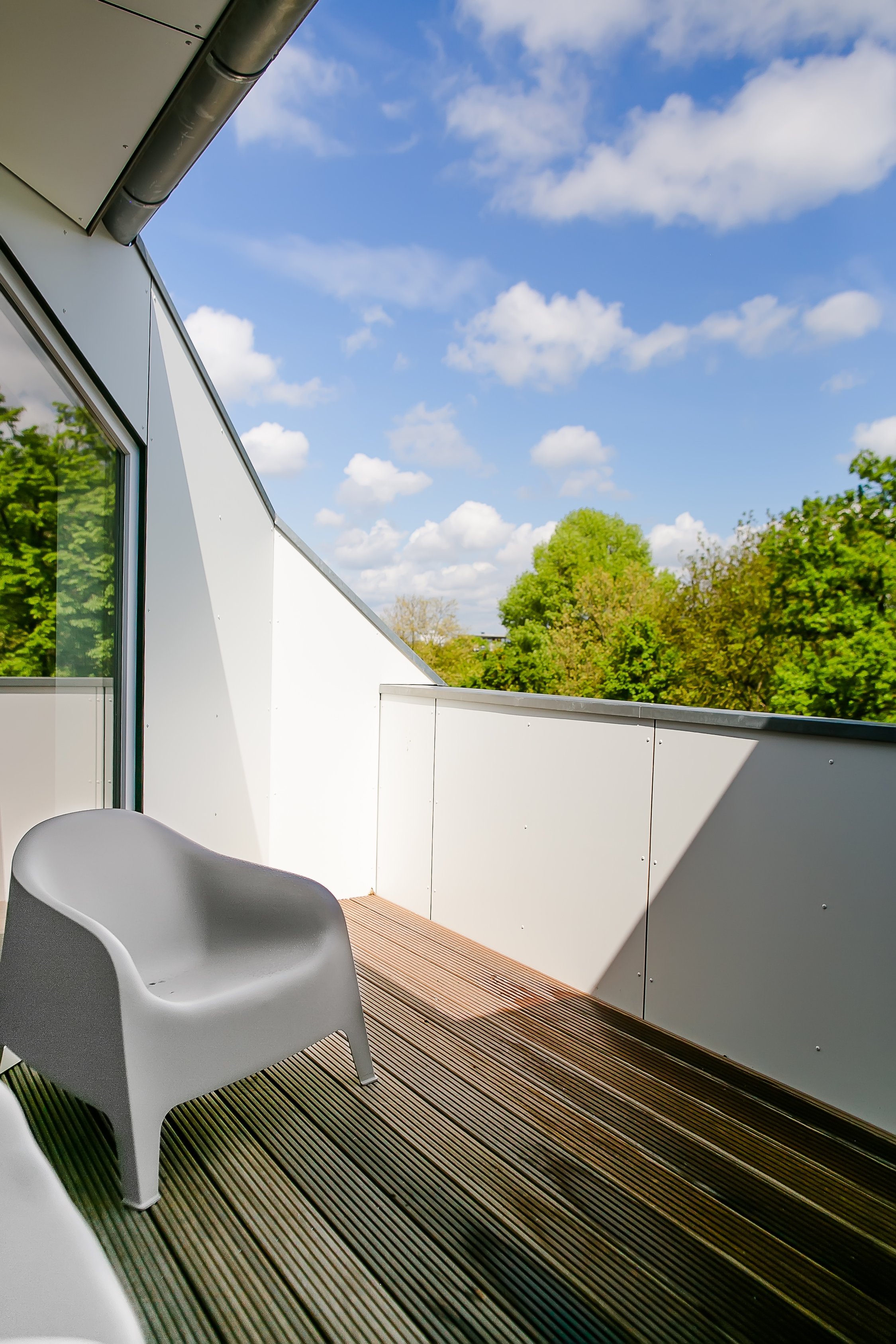 Balkon mit grauen Plastikstühlen, Holzfußboden, weißer Brüstung und blauem Himmel