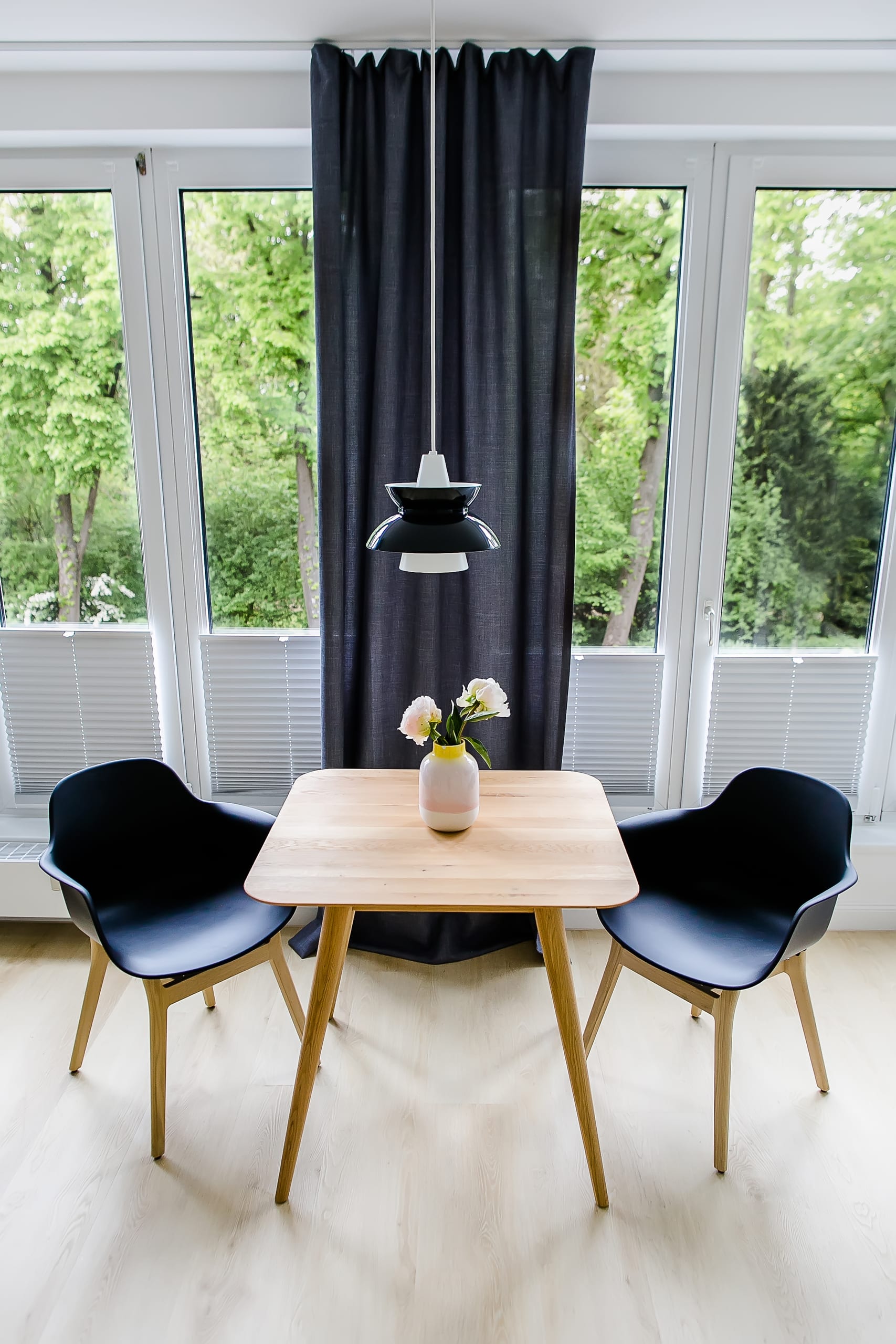 Kleiner Holztisch mit zwei schwarzen Stühlen, großer Fensterfront und Hängelampe