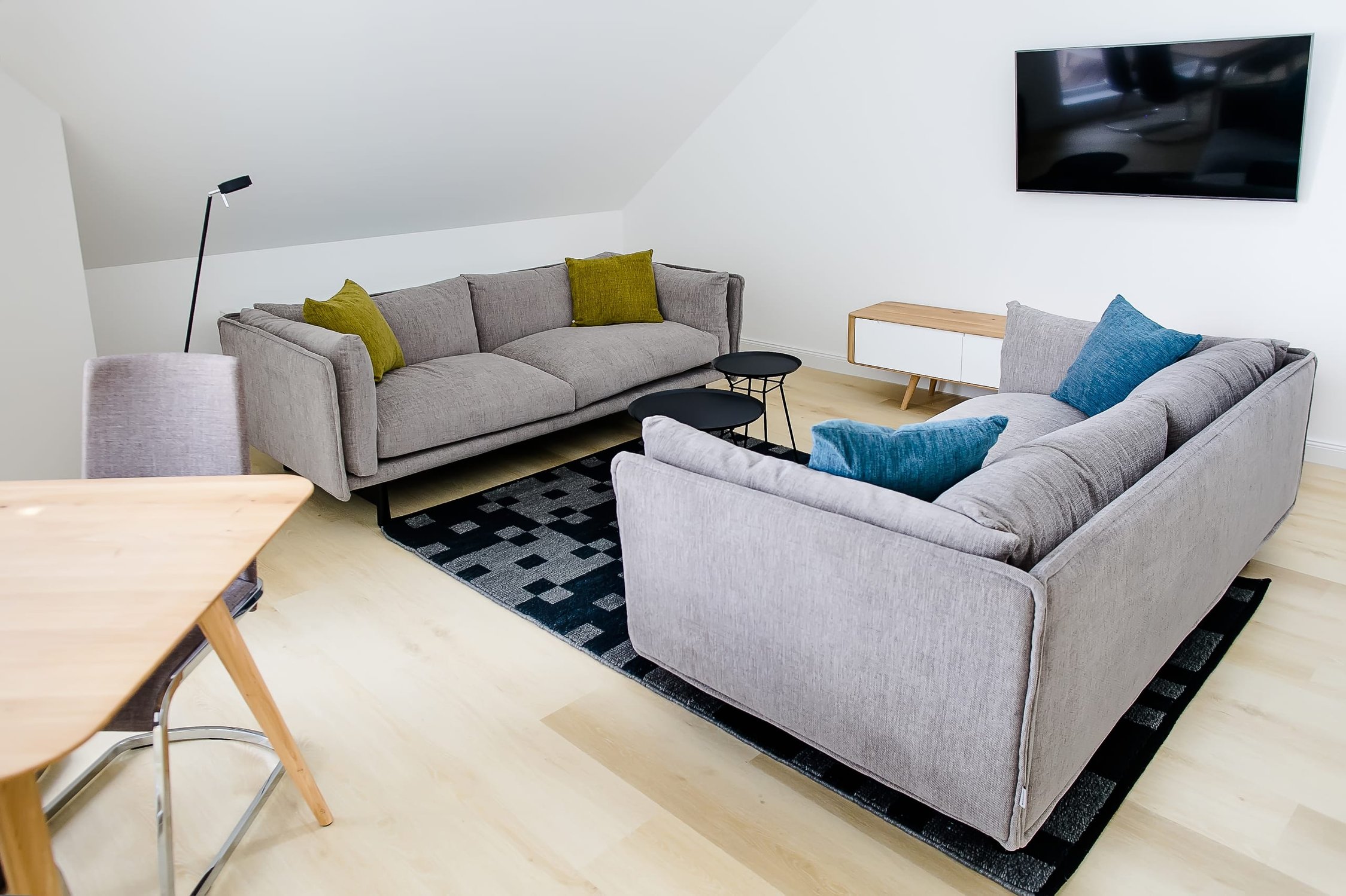 Helles Wohnzimmer mit zwei grauen Sofas auf Teppich, Holzboden, Fernseher an Wand
