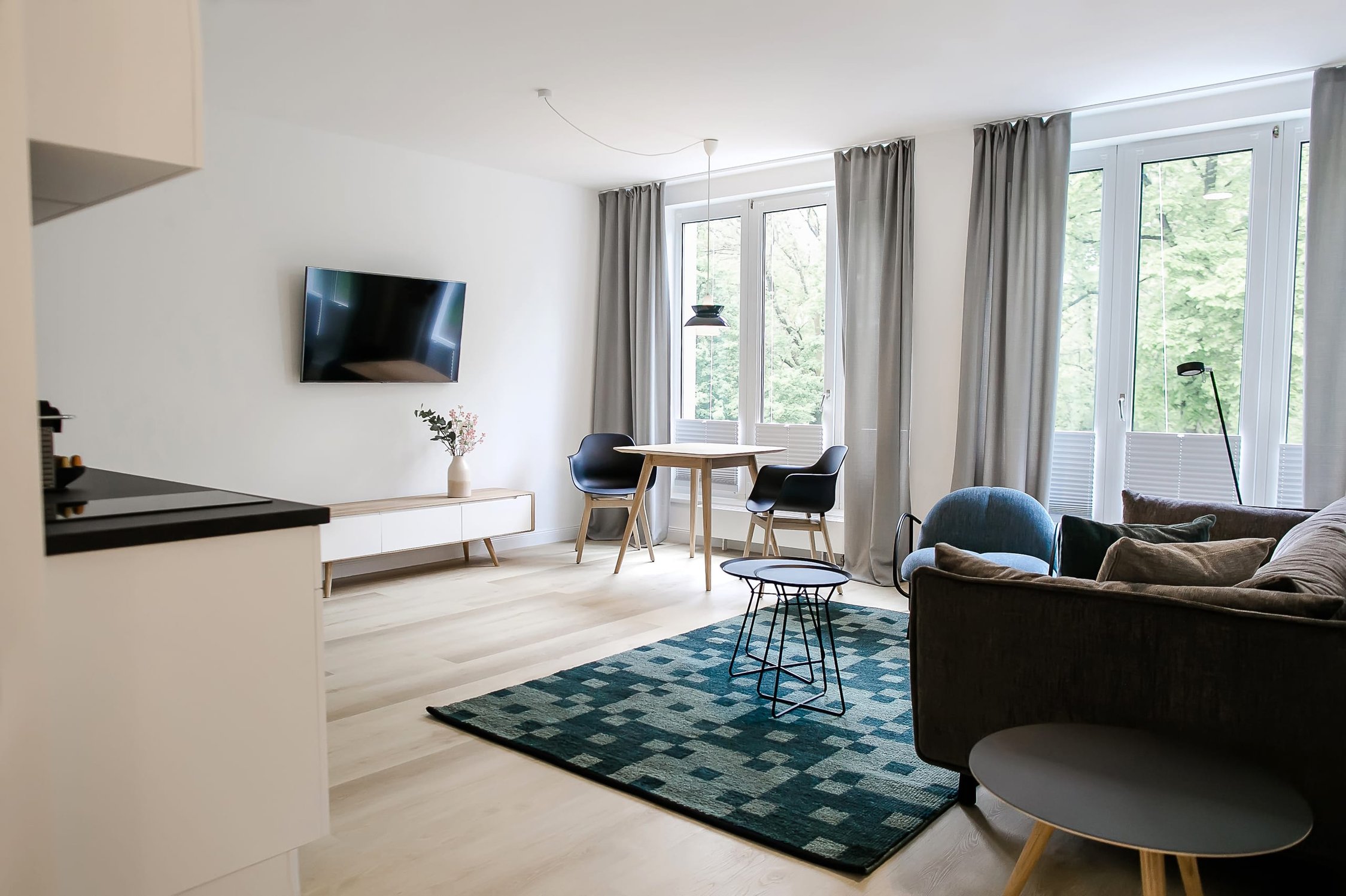 Modernes Wohnzimmer mit hellem Holzboden, TV, dunklem Sofa und Esstisch am Fenster