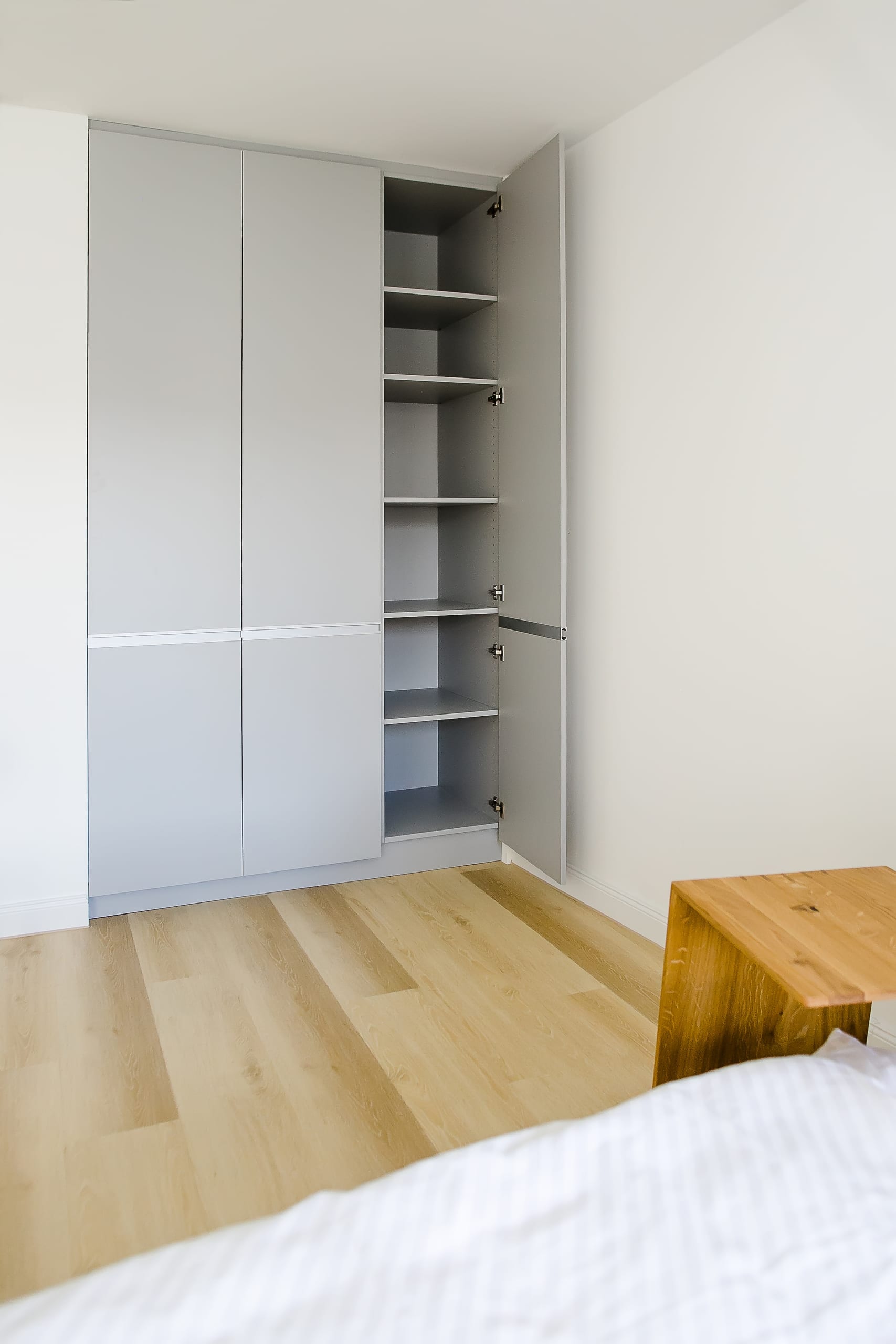 Heller Raum mit hellem Holzboden, weißem Wandschrank und offener Tür mit Regalen