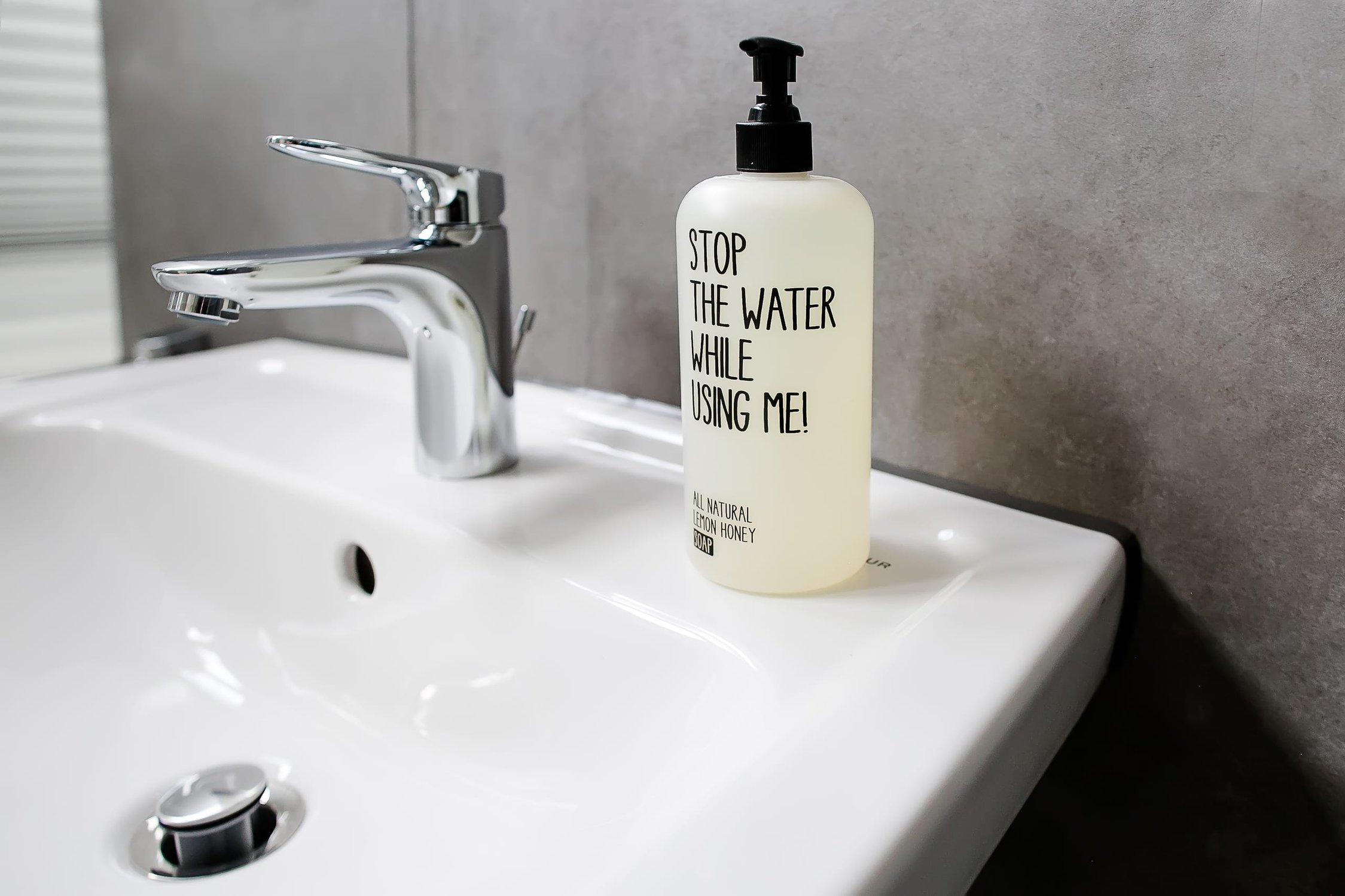 Badezimmerwaschbecken aus weißer Keramik mit Chromarmatur und einer Flasche Seife